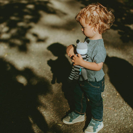 Child holding a stuffed raccoon in a park setting