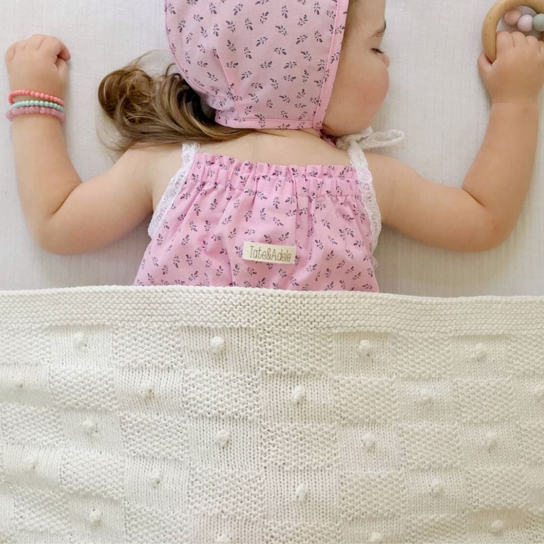 Child wearing a pink floral dress lying on a textured white blanket