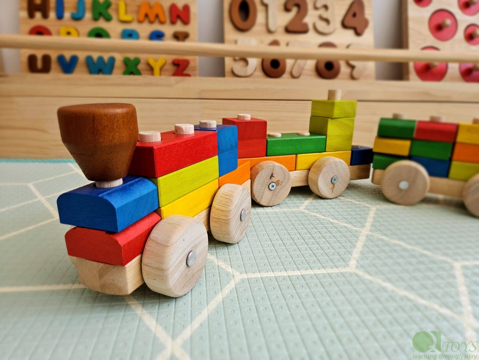 Colorful wooden block train on a green mat with alphabet and number blocks in the background