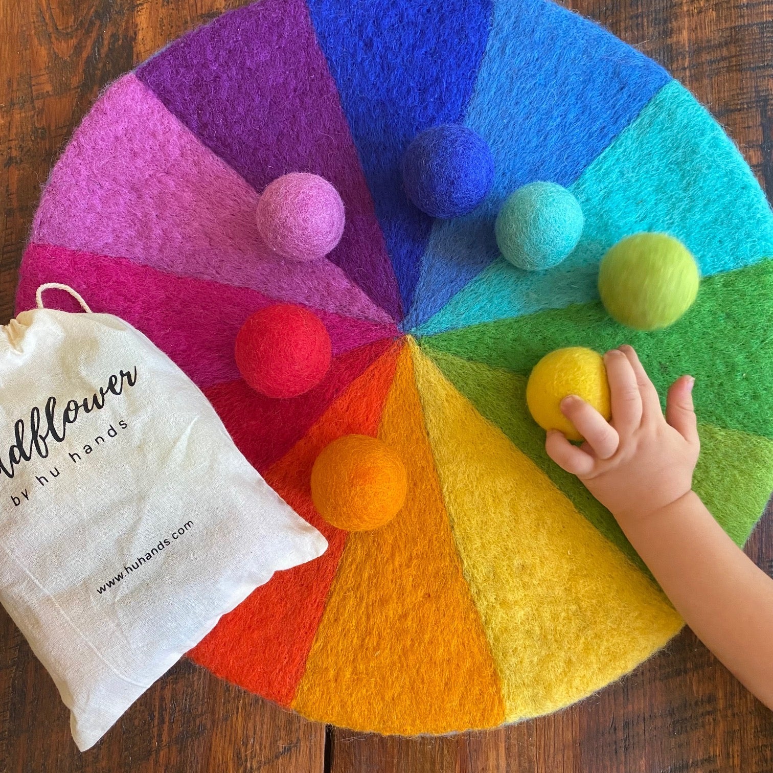 Colorful felt wheel with pom-poms and a child's hand interacting with it on a wooden surface.