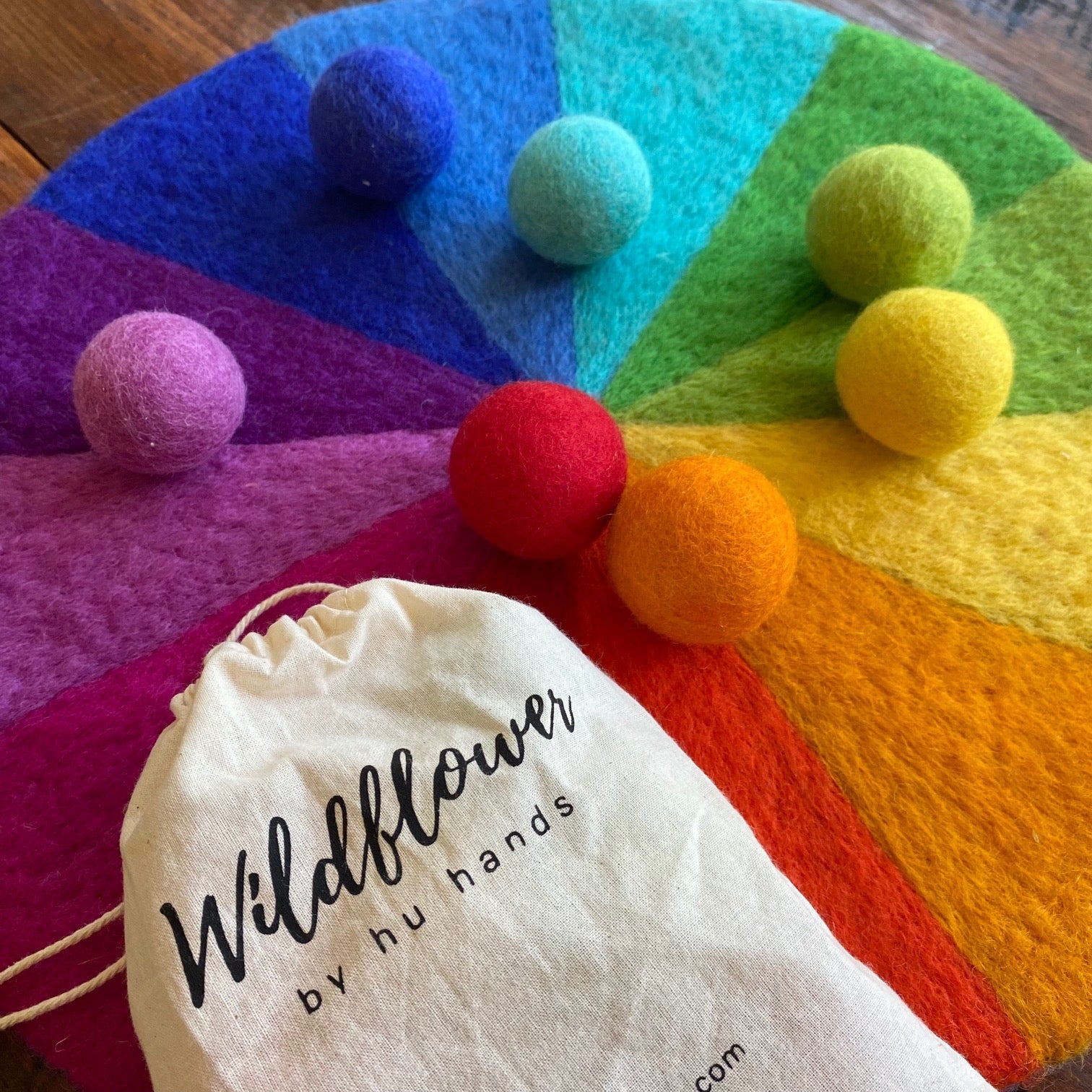 Colorful felt balls on a rainbow-colored surface with a 'Wildflower by hu hands' bag.