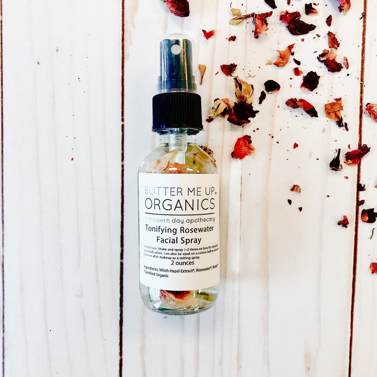 Butter Me Up Organics facial spray bottle on a wooden surface with dried flowers.