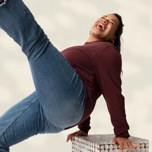 Person in maroon hoodie and blue jeans performing a handstand on a white background