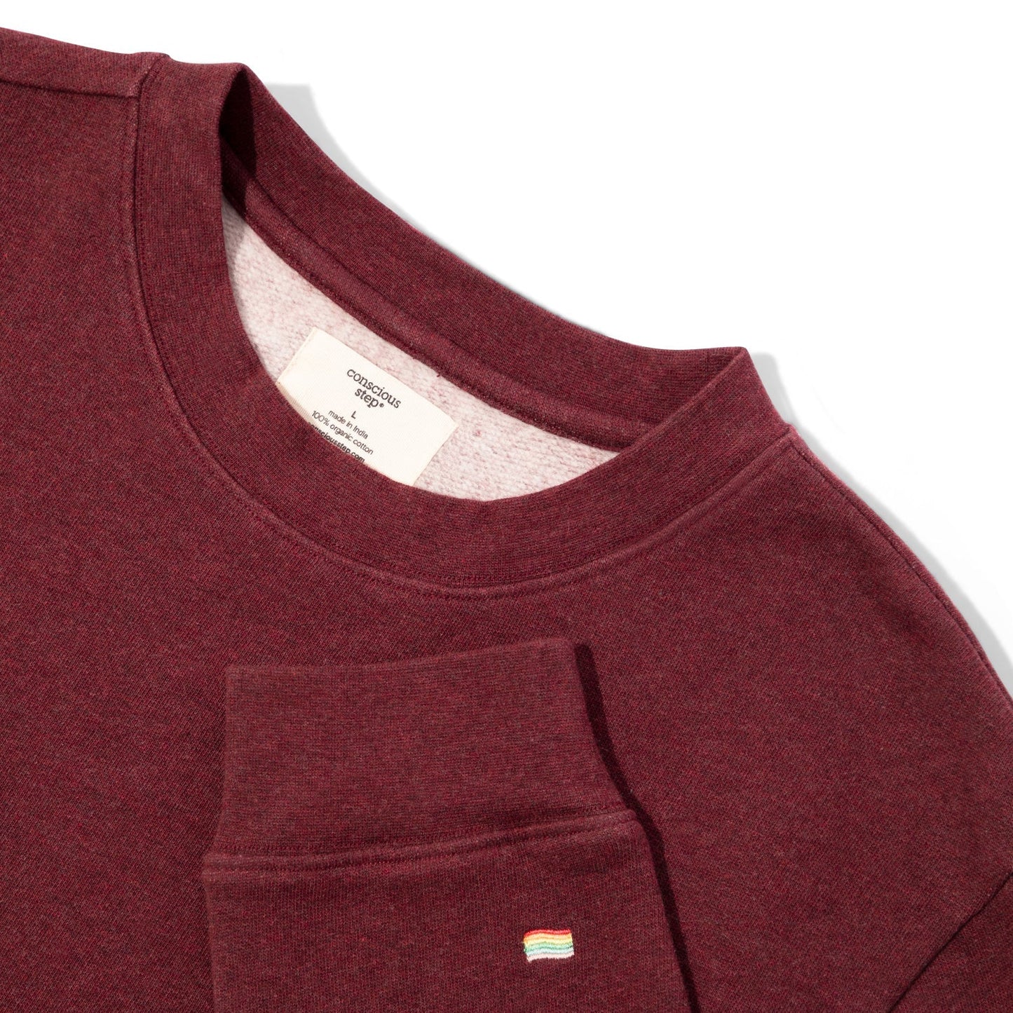 Close-up of a maroon sweatshirt with a brand label and pocket detail on a white background