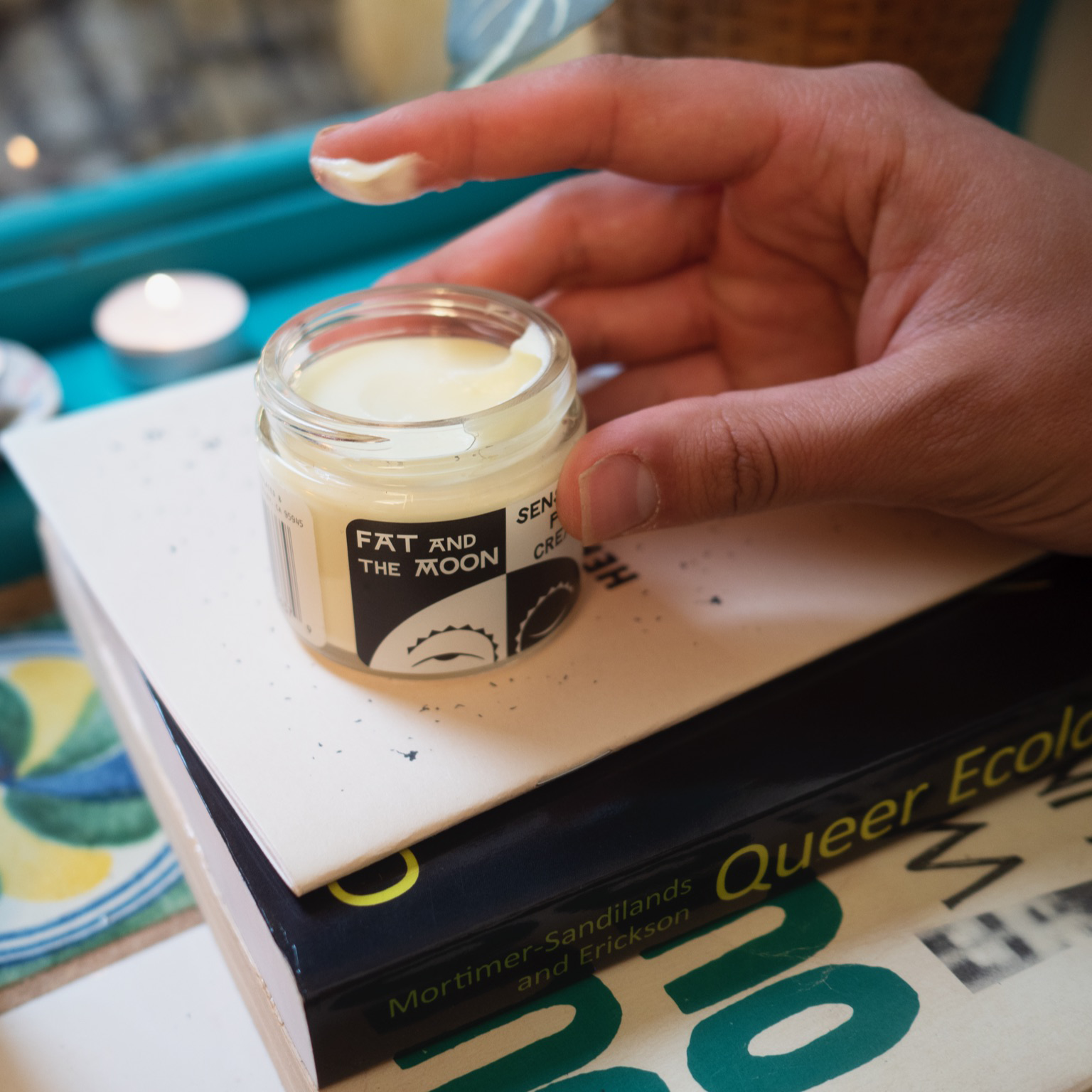Hand holding a jar of cream on top of books