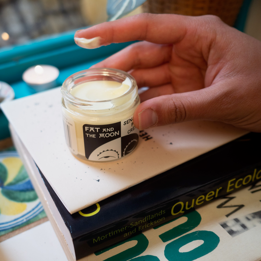 Hand holding a jar of cream on top of books