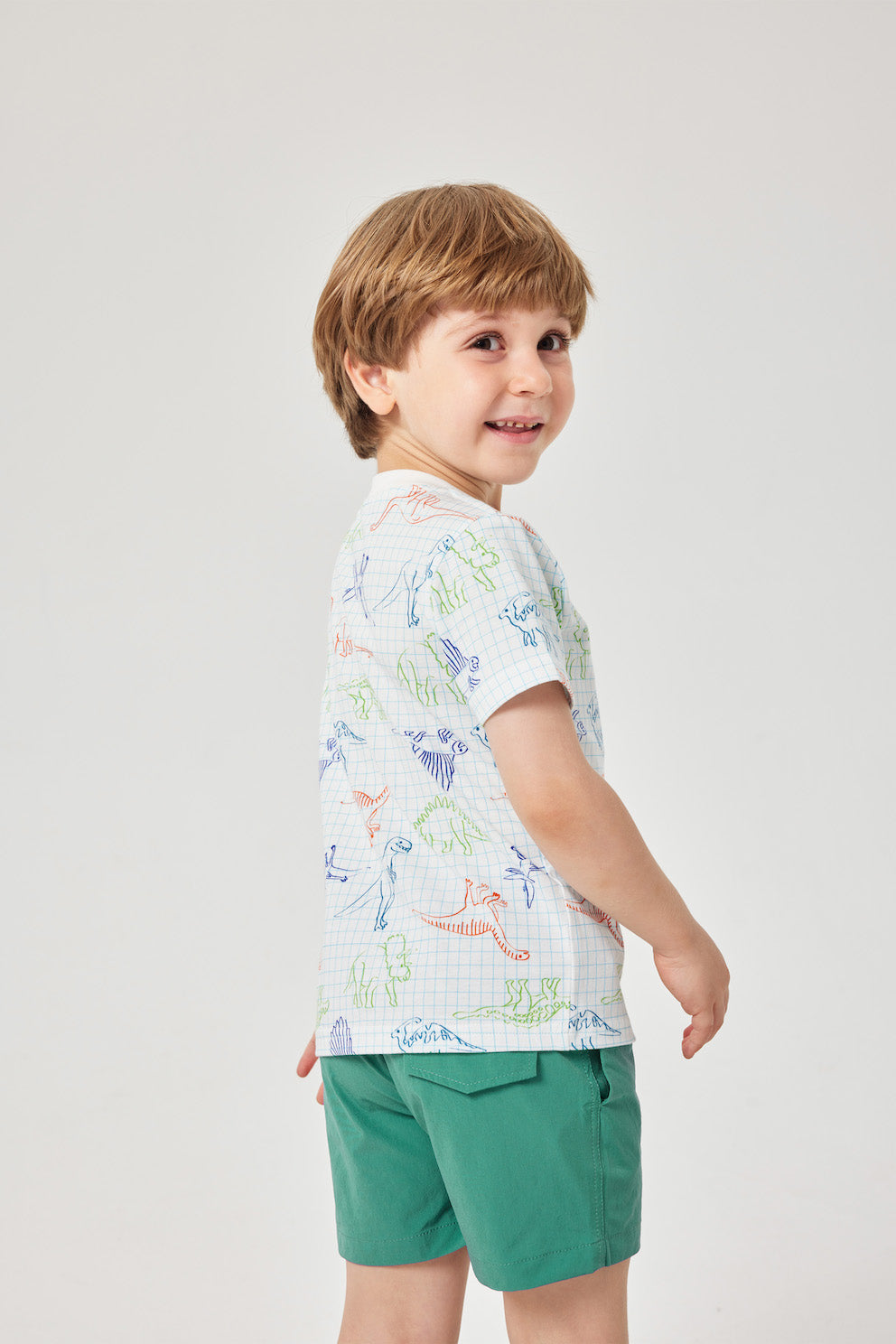Child wearing a patterned shirt and green shorts on a white background