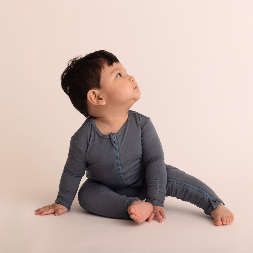 Baby wearing a gray onesie sitting on a beige background