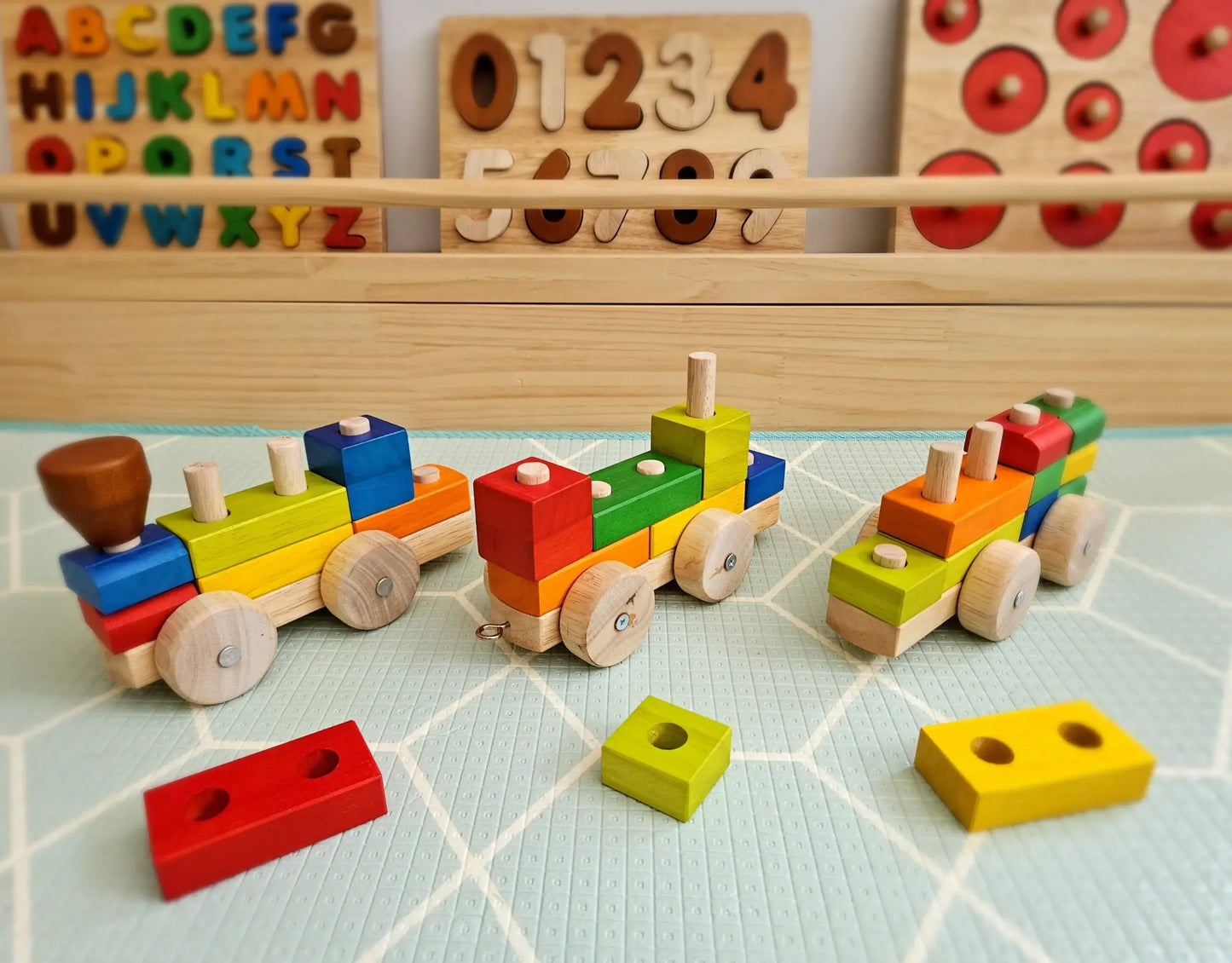 Colorful wooden toy train set on a checkered surface with educational tools in the background.