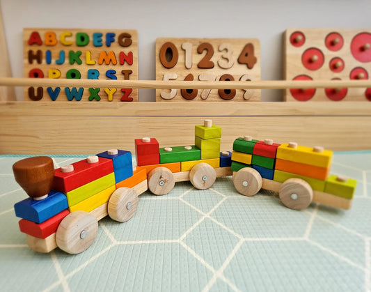 Colorful wooden toy train set on a checkered surface with educational tools in the background.
