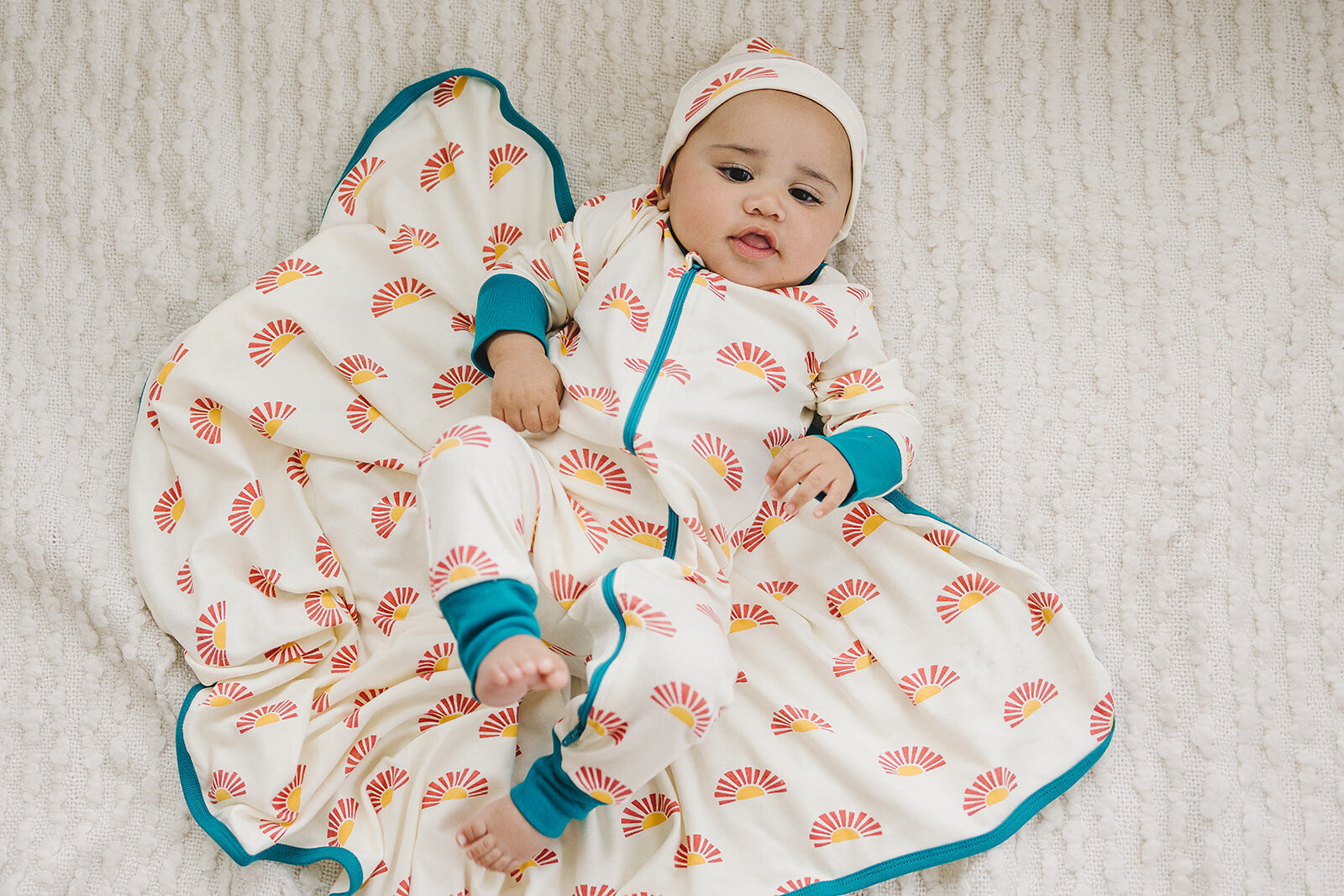 Baby in a patterned onesie and hat sitting on a textured surface