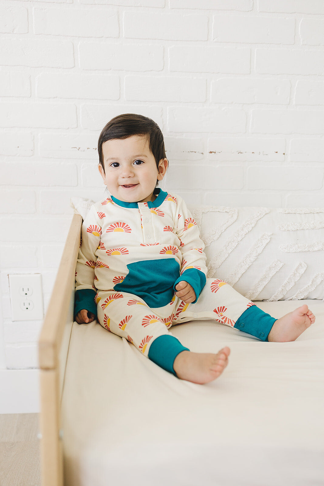 Child wearing colorful pajamas sitting on a couch with a white brick wall background