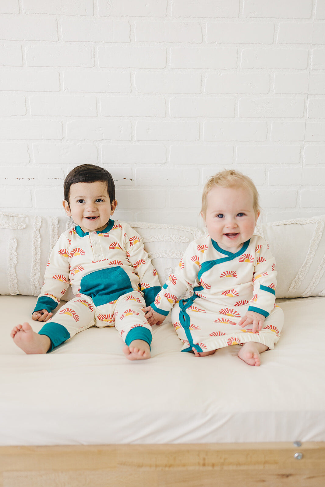 Two children wearing matching pajamas sitting on a couch against a white brick wall.