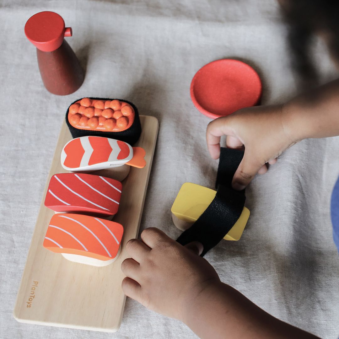 Children playing with a toy sushi set on a wooden board.