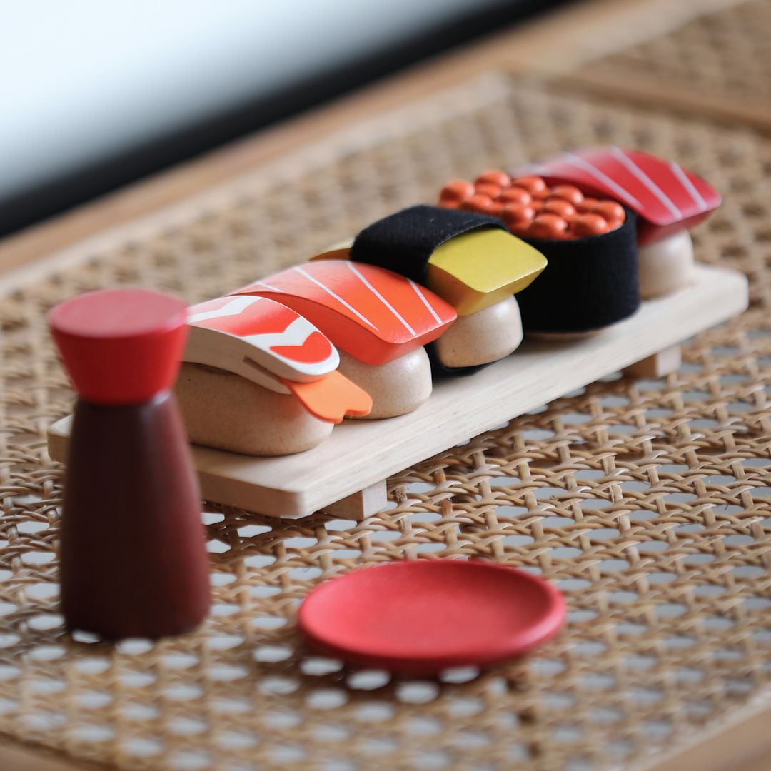 Model of sushi set on a wooden board with a small bottle and plate on a woven mat.