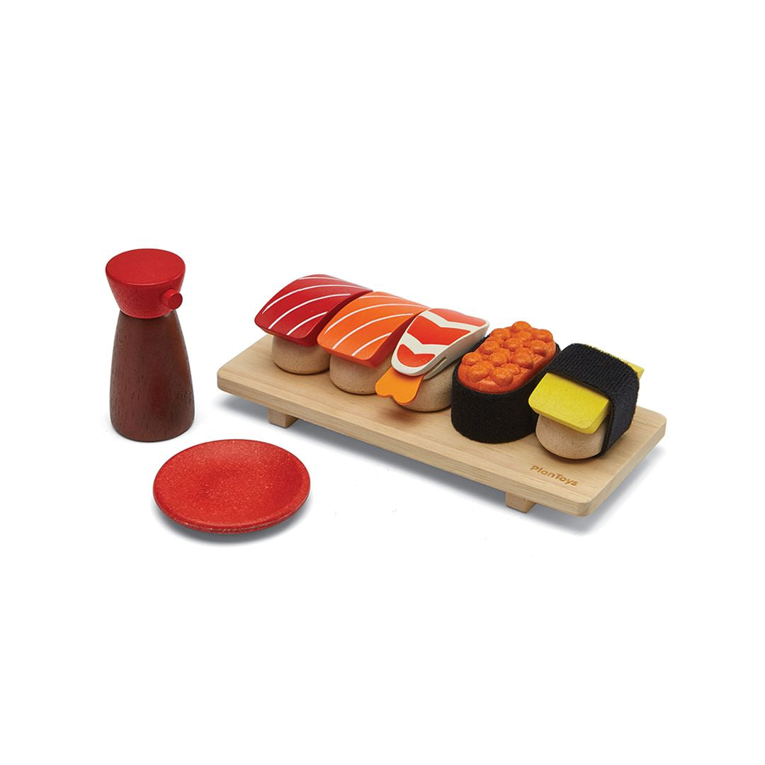 Wooden toy sushi set with a wooden board, soy sauce bottle, and red plate on a white background
