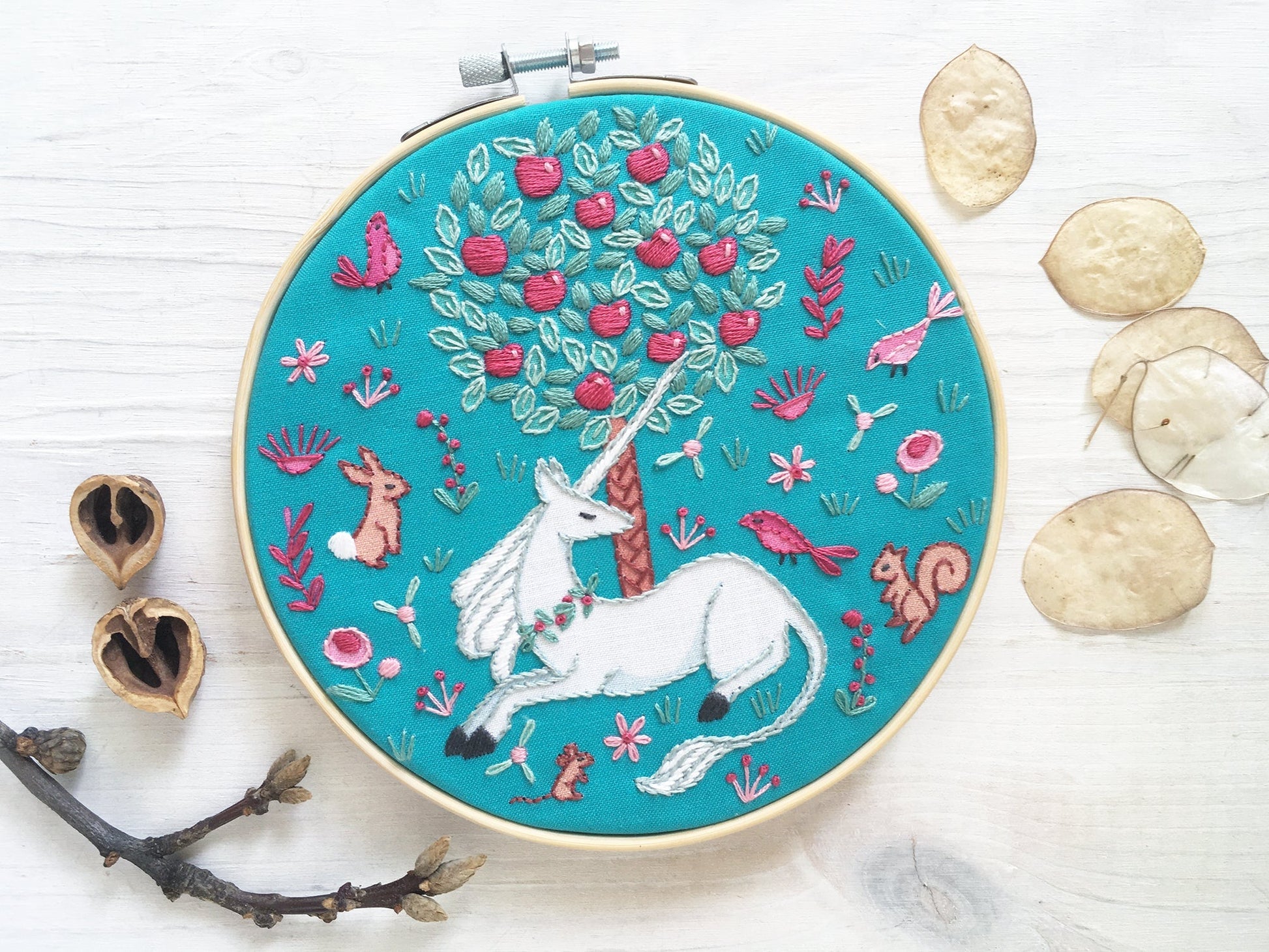 Embroidery hoop with a unicorn design on a blue background, surrounded by natural elements.