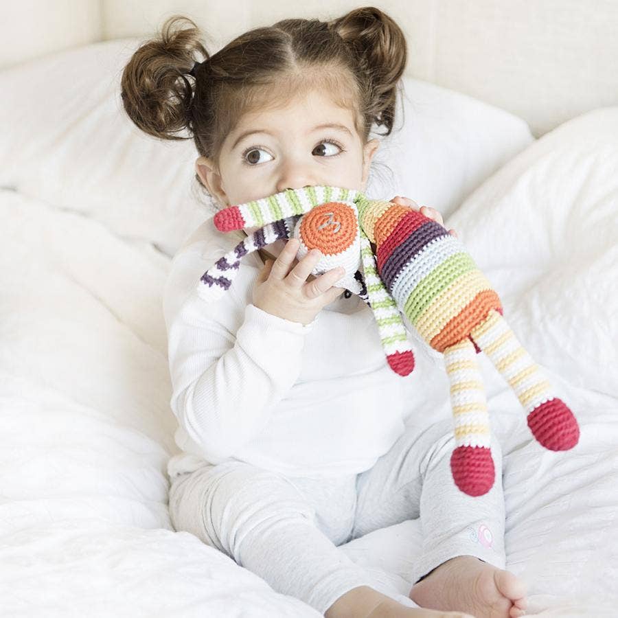 Child holding a rainbow striped bunny on a white bed