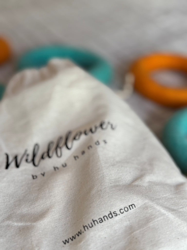 Close-up of a white drawstring bag with 'Wildflower by hu hands' branding, featuring colorful rings in the background.
