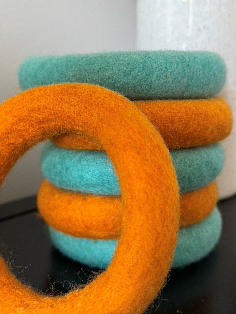 Stack of orange and turquoise felted rings on a dark surface with a white background