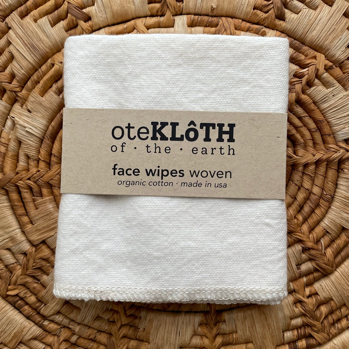 Folded white face wipes with a brown label on a woven mat