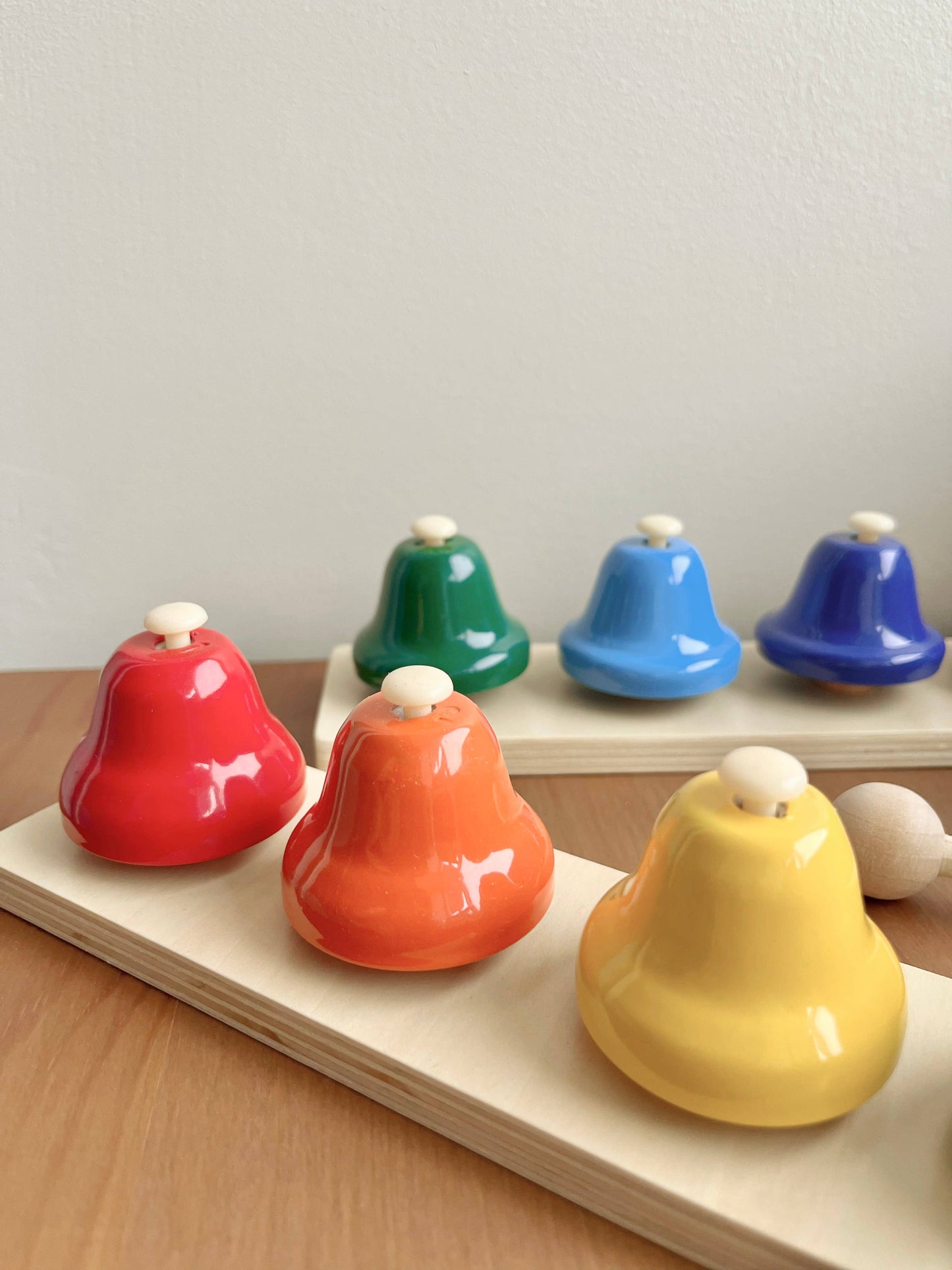 Set of colorful metal bells on a wooden stand against a light background