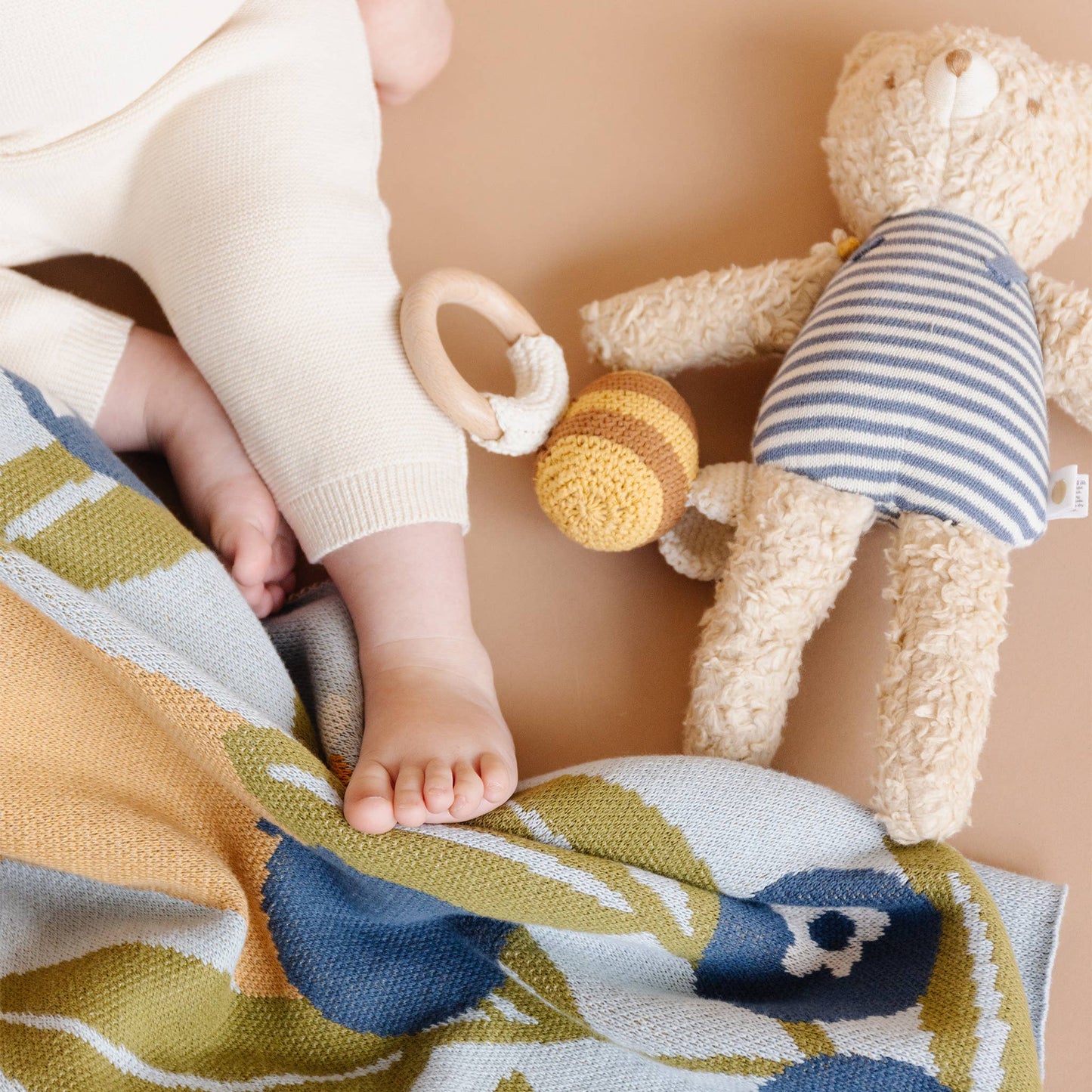 Baby's foot near a soft bear toy and a crochet bee teether on a colorful blanket