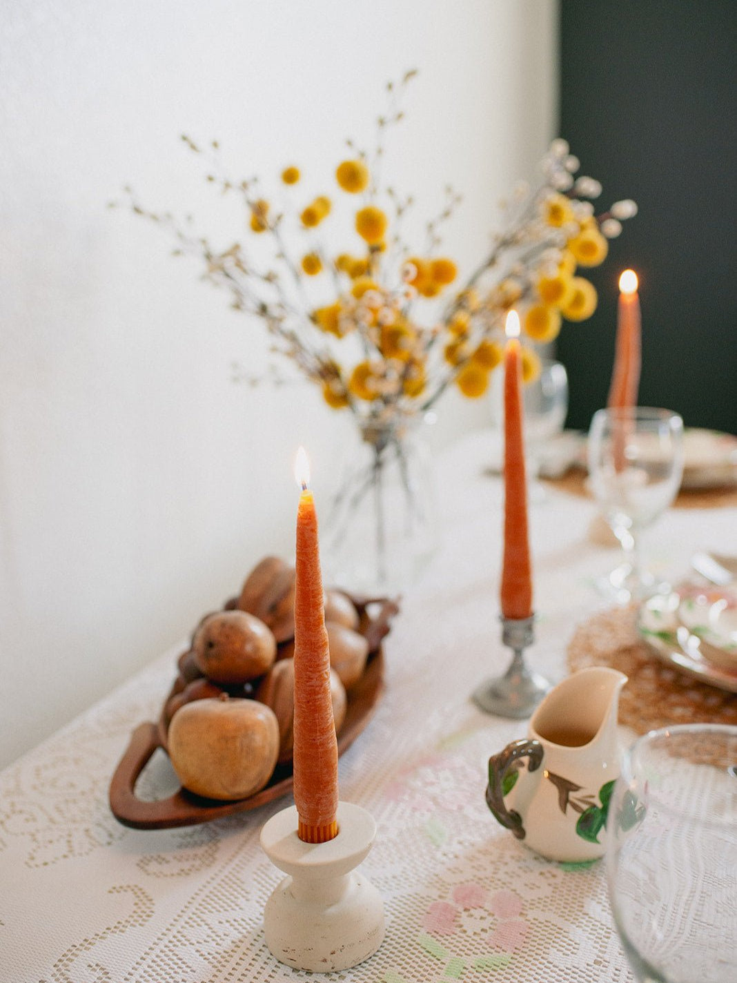Decorative table setting with orange candles, flowers, and a teapot on a white tablecloth.