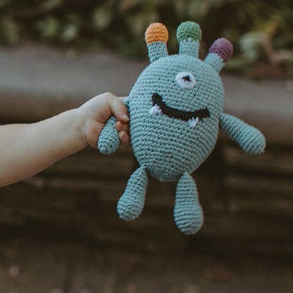 Hand holding a crocheted monster toy with colorful hair against a blurred natural background