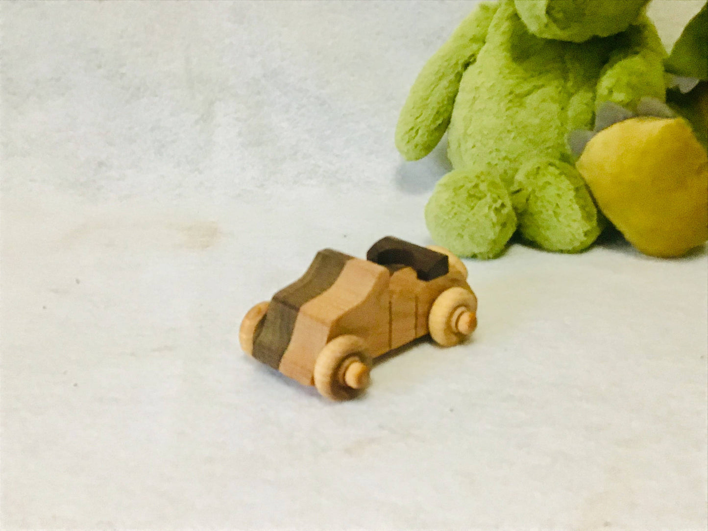 Wooden toy convertible next to a green plush toy on a light background