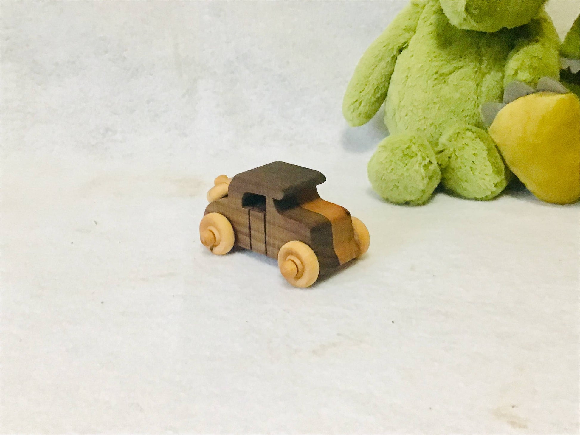Wooden toy jeep next to a green plush toy on a white surface