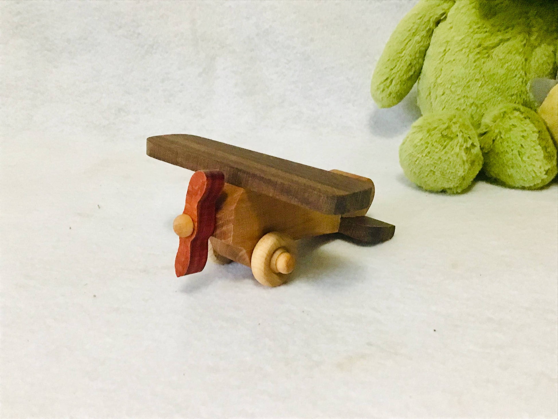 Wooden toy airplane on a white surface with a green plush toy in the background