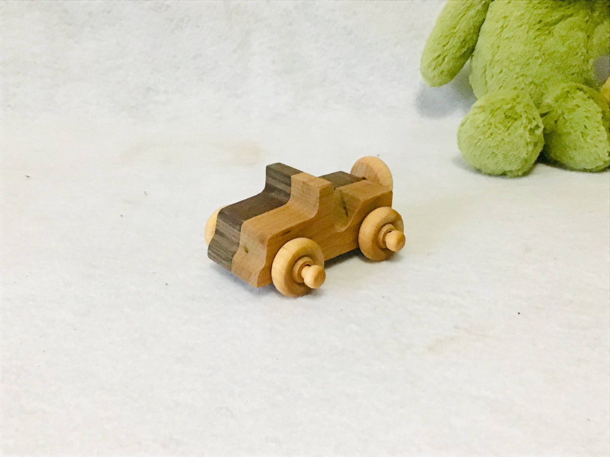 Wooden toy sports car next to a green plush toy on a white surface