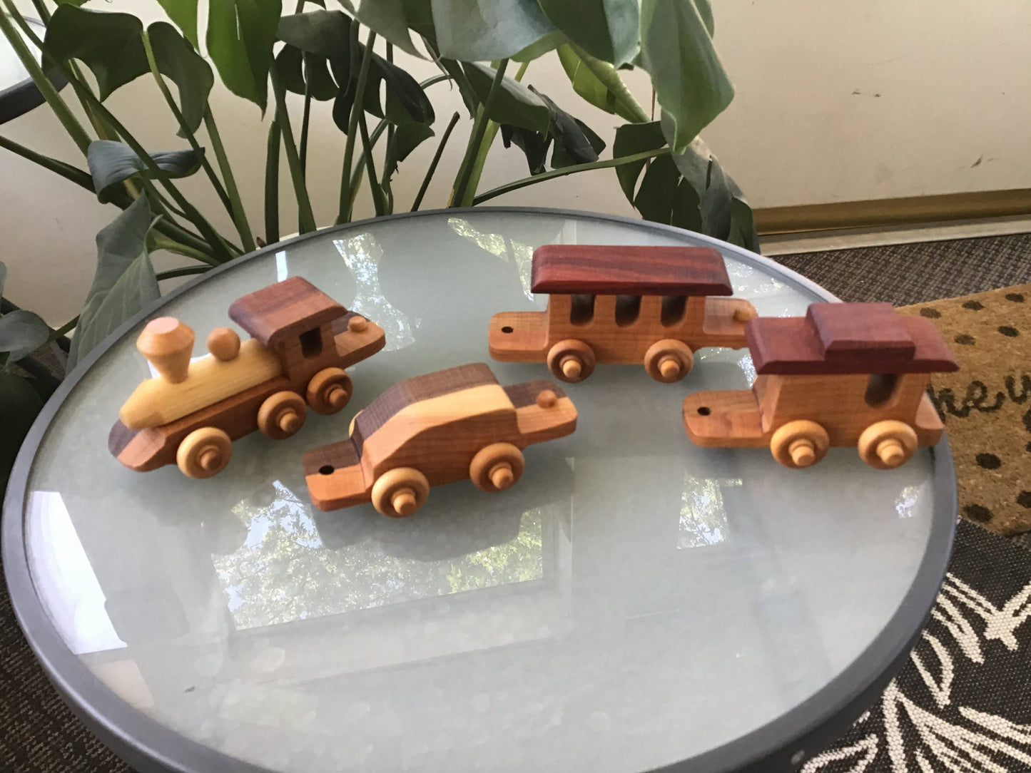 Wooden toy train set on a round glass table with plants in the background