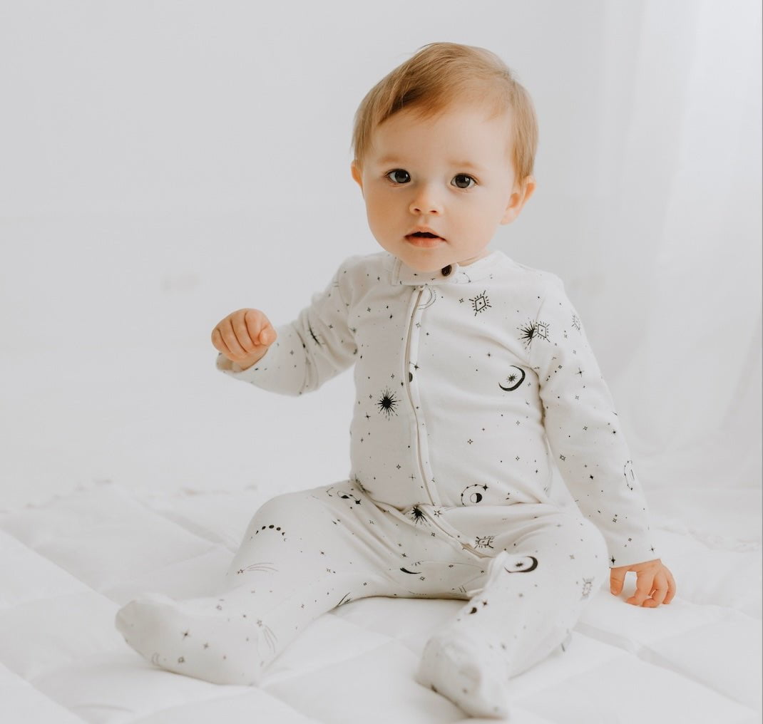 Baby wearing a white onesie with black patterns on a light gray background