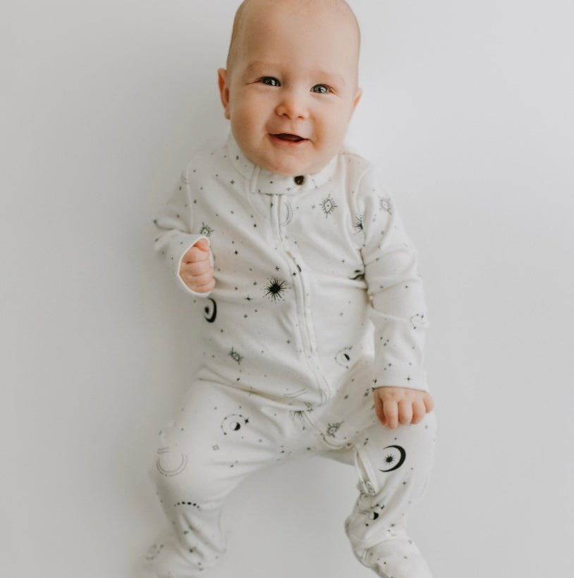 Baby wearing a white onesie with black patterns on a plain background