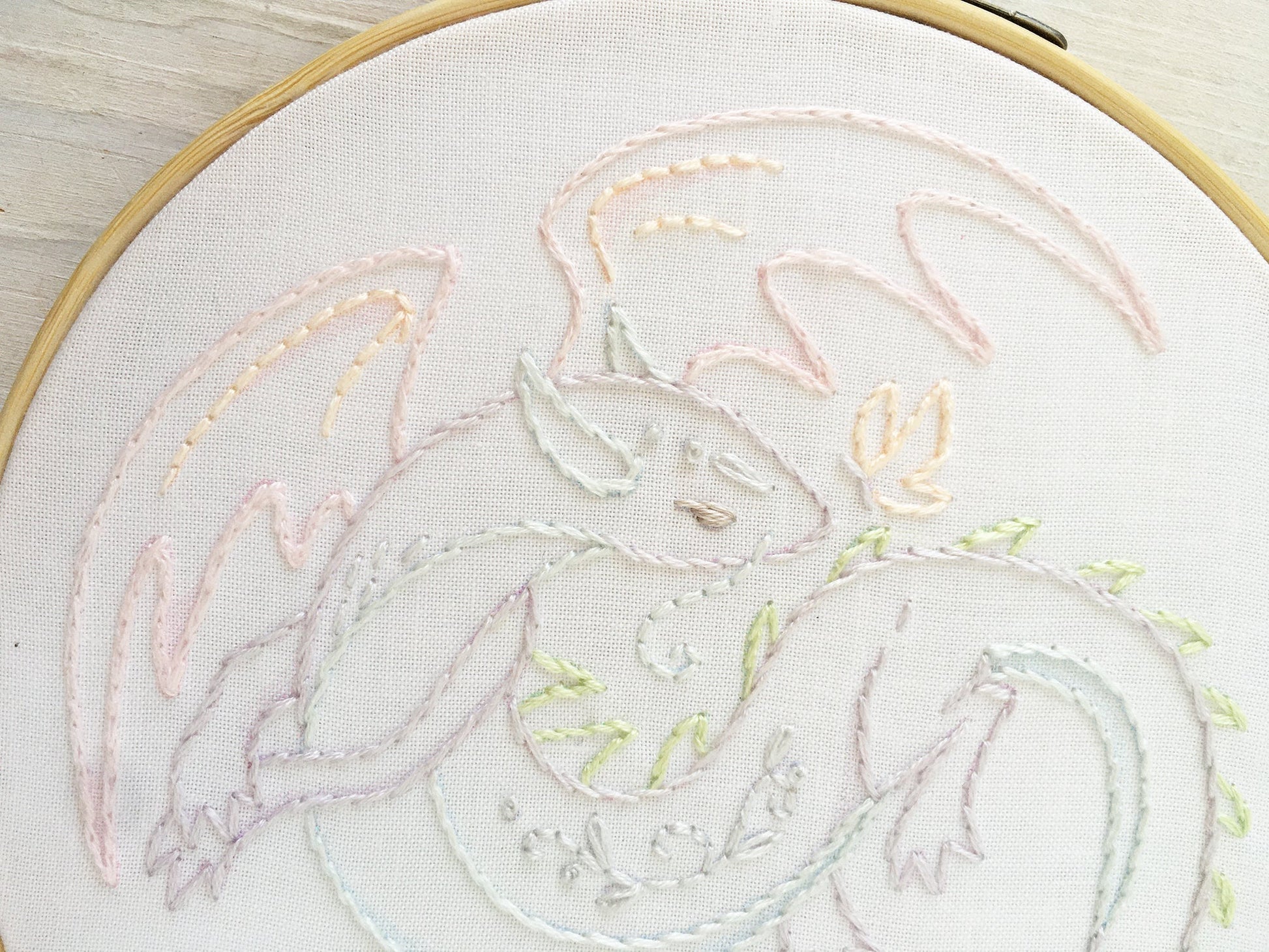 Embroidery of a dragon design on white fabric with a wooden hoop.