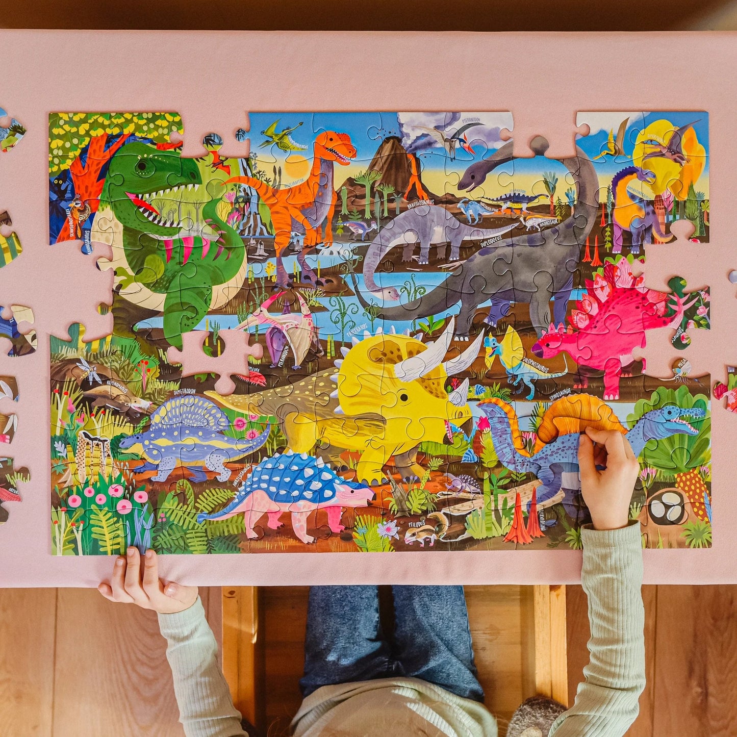 Child assembling a dinosaur-themed puzzle with colorful illustrations on a pink table.