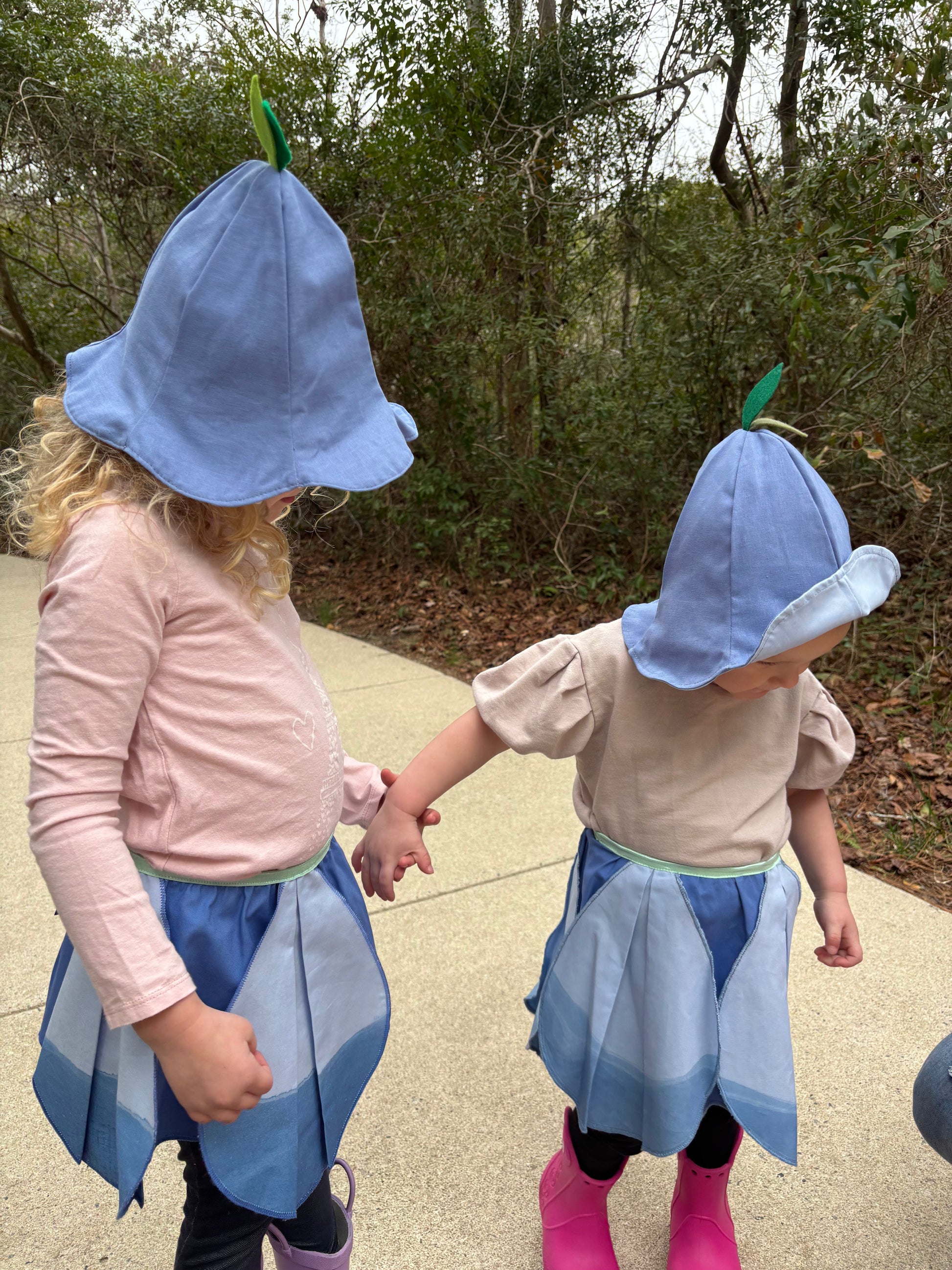 Two children in blue costumes with hats and aprons standing outdoors on a path.
