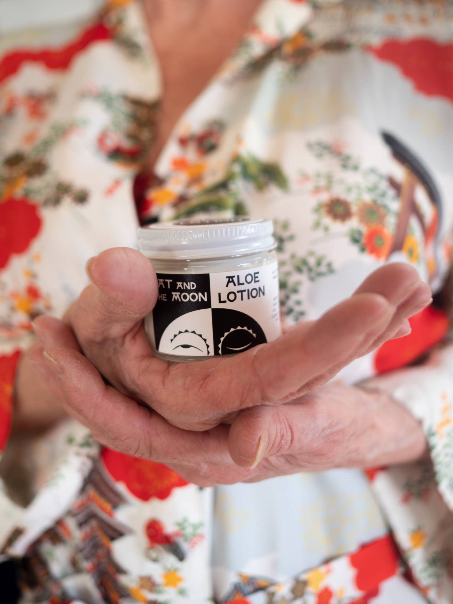 a person wearing a flower shirt holding a tub of aloe lotion in their hands