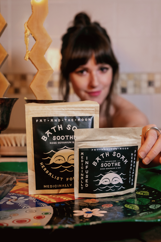 a person sitting in a bathtub holding a bag of soothe bath soak