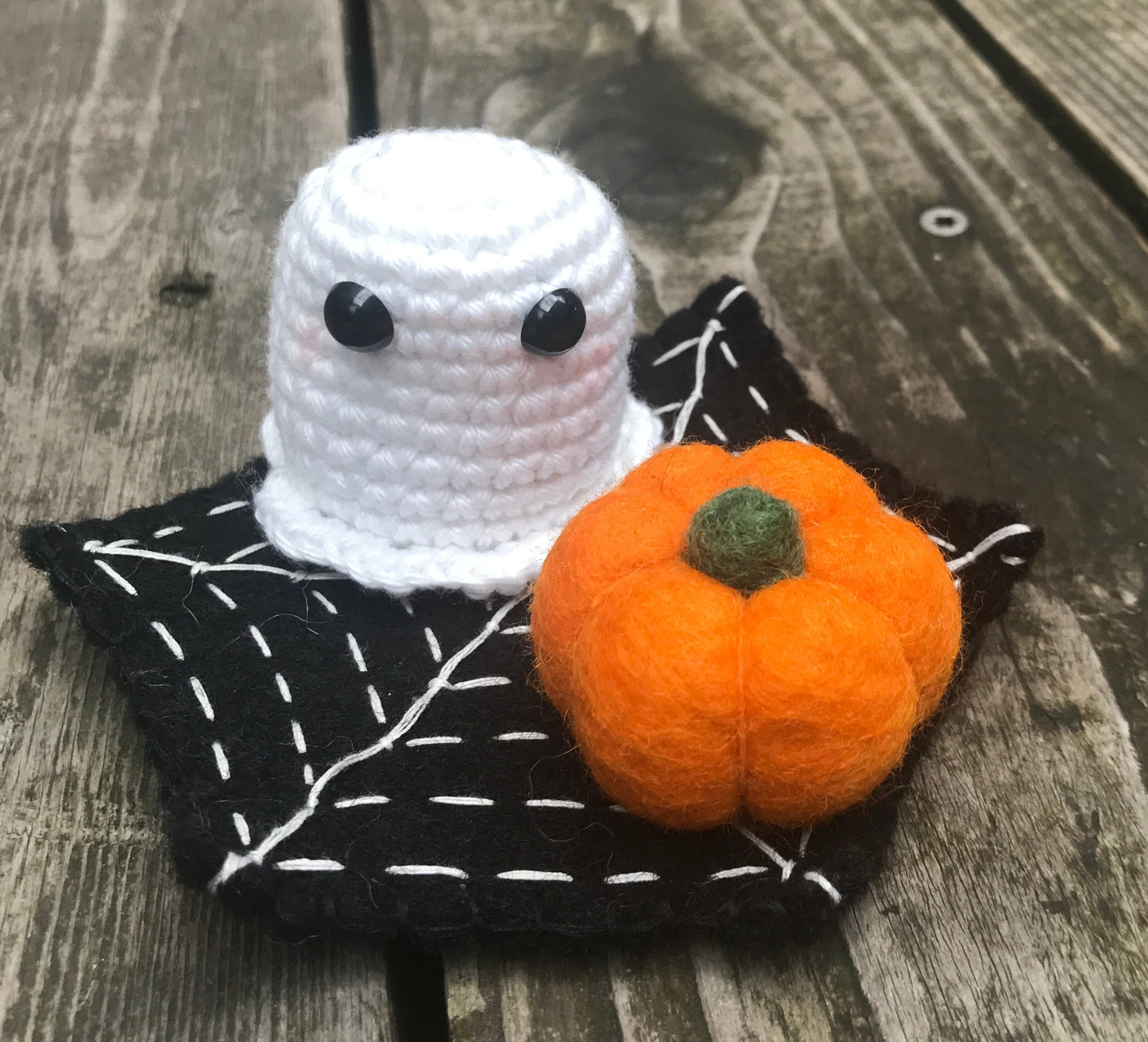 Crocheted ghost with a small pumpkin on a felt spider web