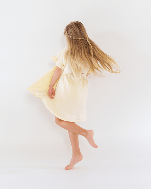 Child in a yellow dress standing on a white background