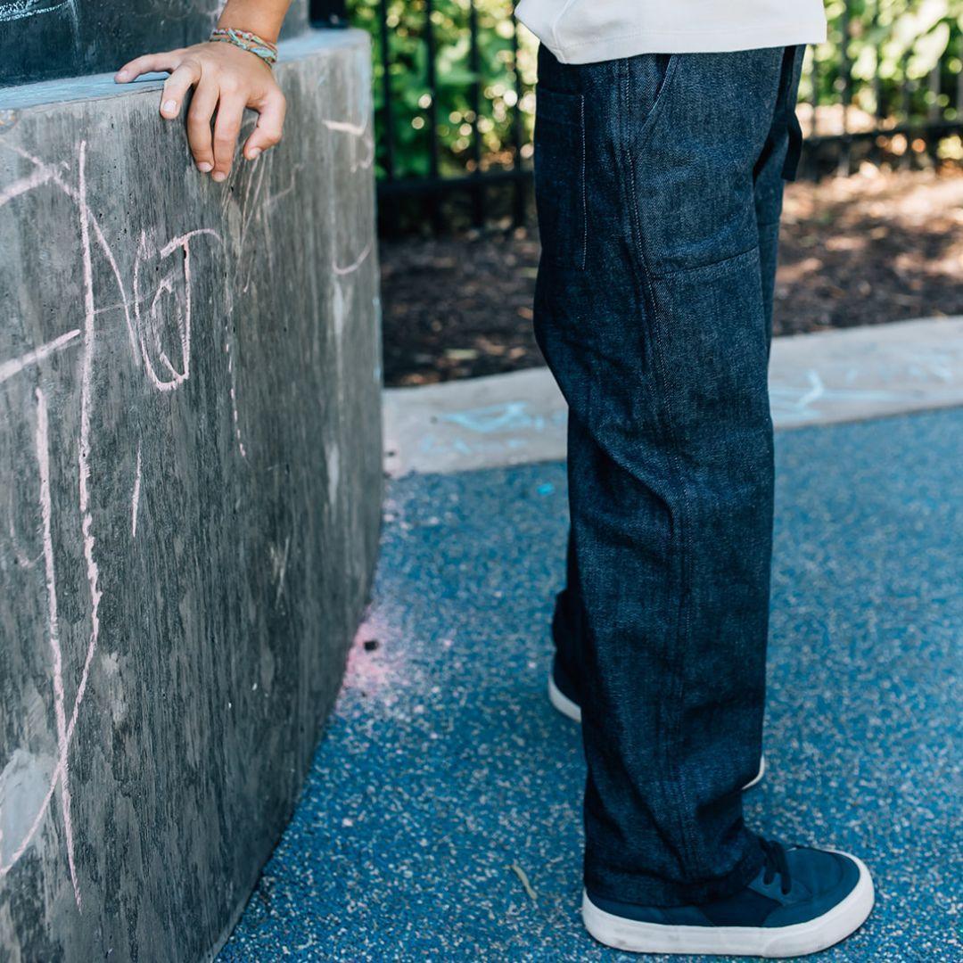 Person wearing dark blue jeans standing next to a chalkboard with outdoor background