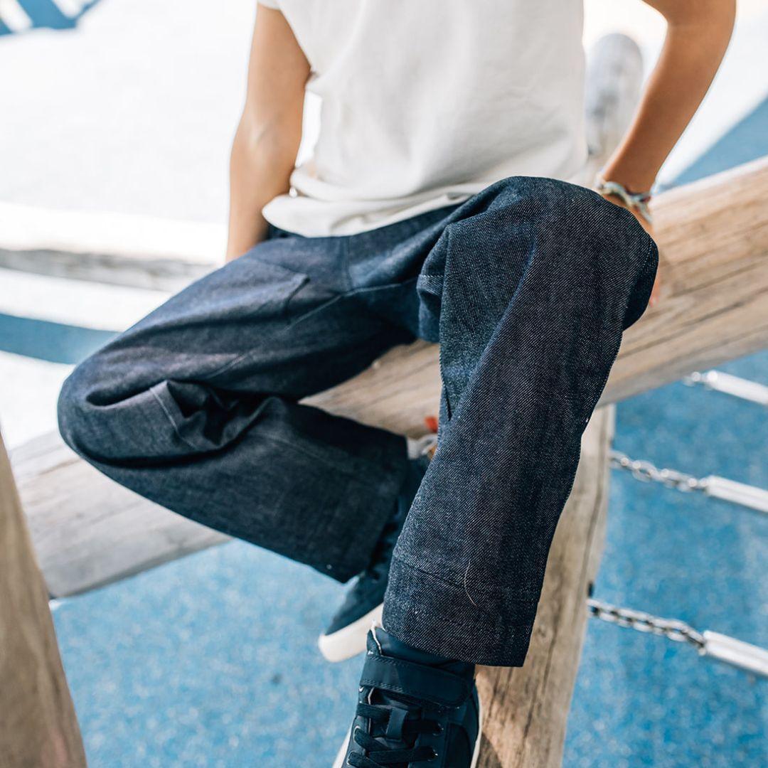 Person wearing dark blue jeans sitting on a wooden railing with a blurred background
