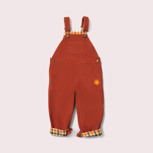 Rust corduroy overalls with plaid lining on a light beige background