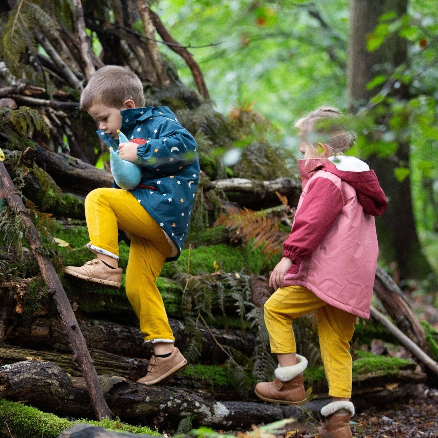 Two children walking through the woods wearing recycled winter coats