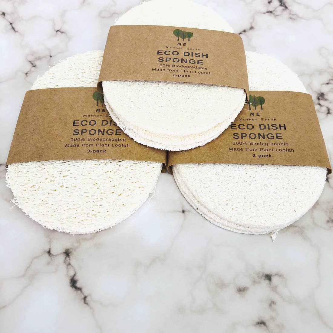Three eco dish sponges with brown paper packaging on a marble surface