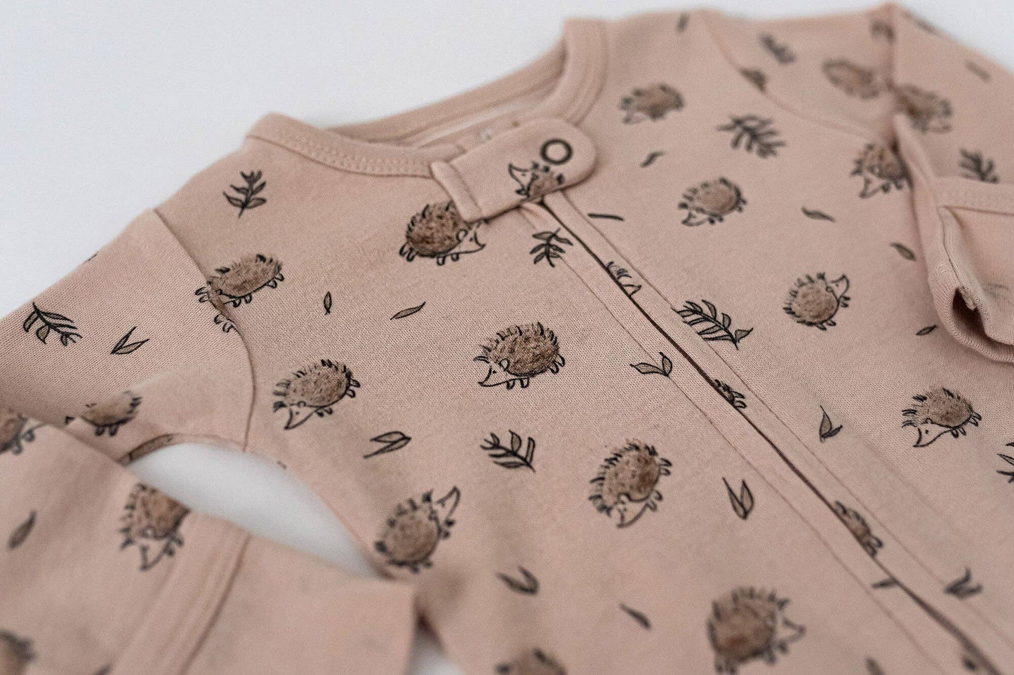Beige baby romper with hedgehogs pattern on a white background