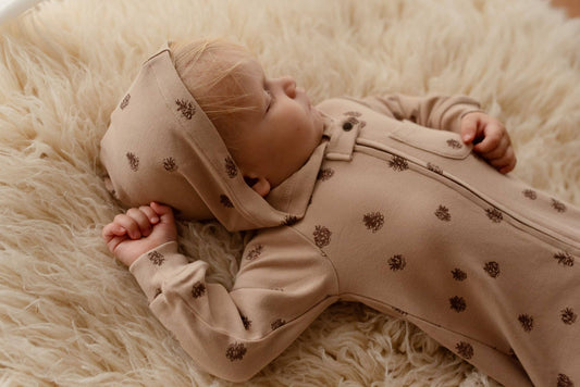 Baby in a beige romper with pinecones patterns lying on a fluffy white surface